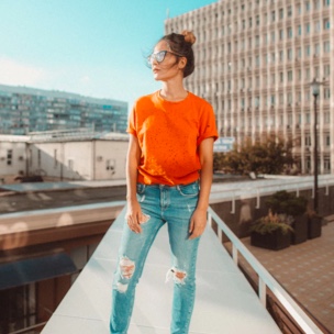 Sophie standing infront of city buildings wearing orange shirt and jeans