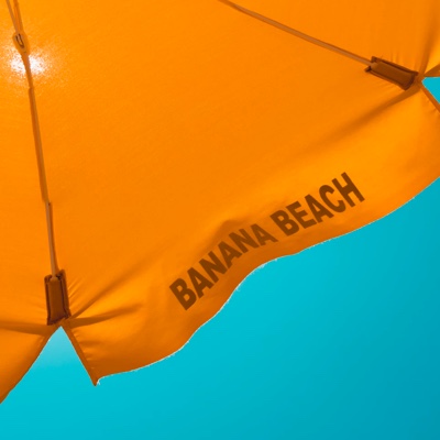 Orange umbrella with banana beach printed on it